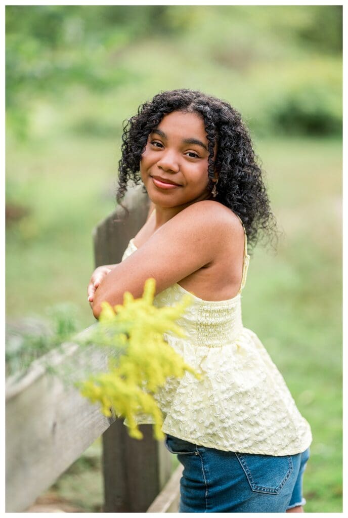 Bright and airy portrait of senior leaning by wooden railing at park.