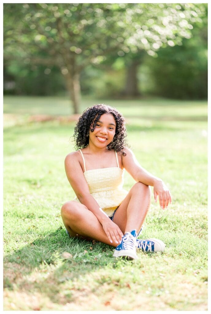 Andover High Senior sitting in grass smiling gently during bright Massachusetts portrait session.