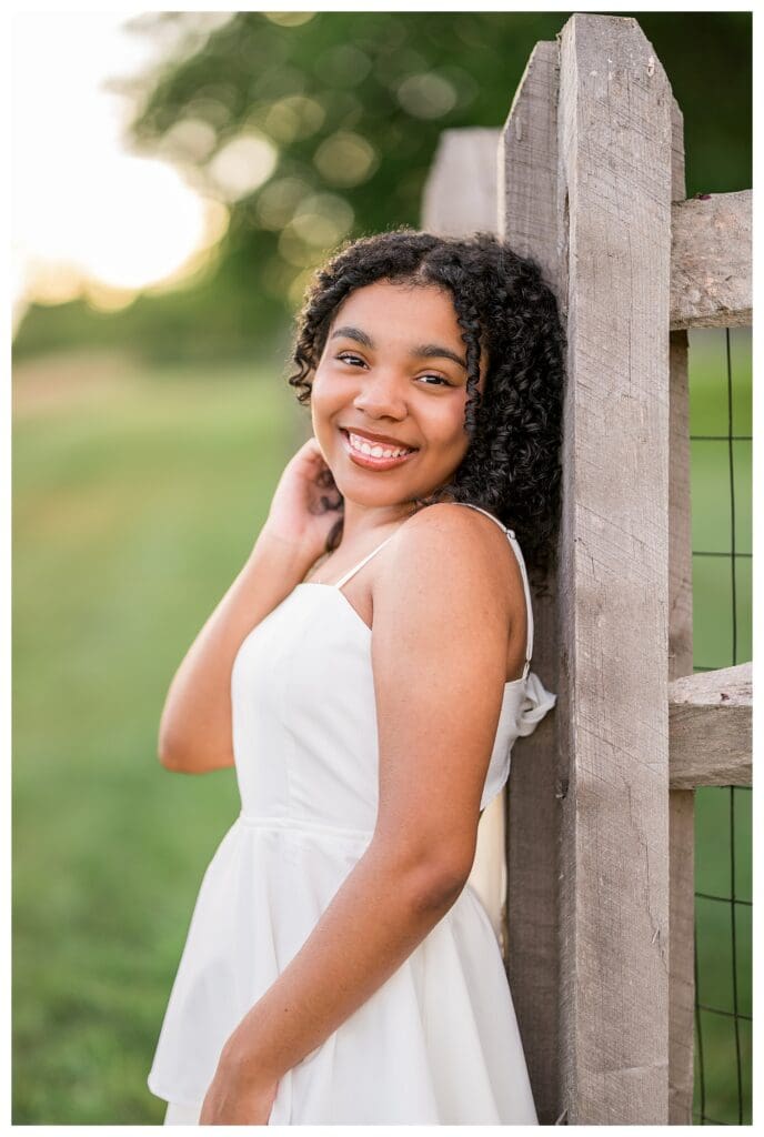 Senior girl smiling confidently near rustic wooden fence during Andover High School senior photos.