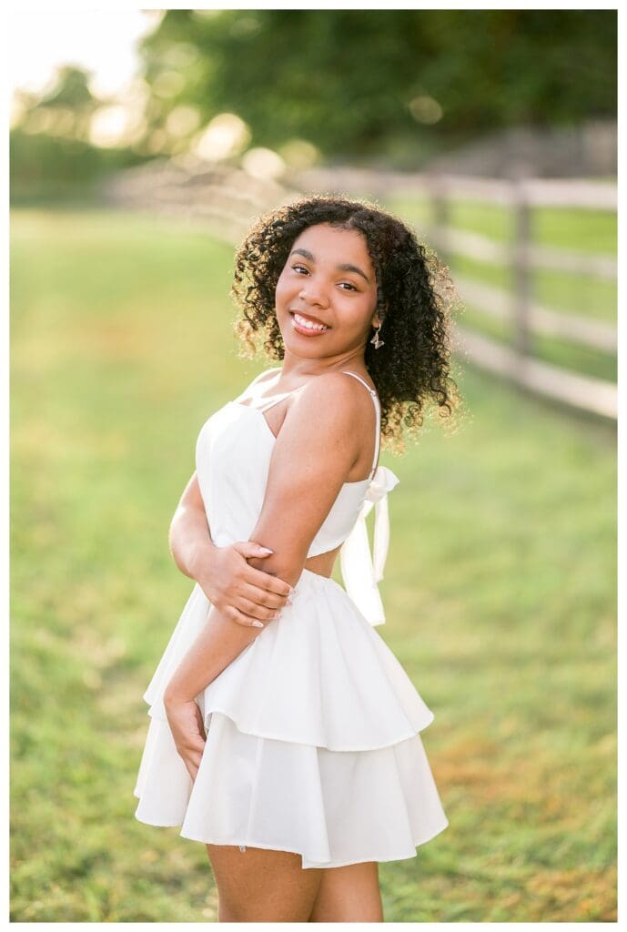 High school dancer posing gracefully in white dress outdoors.