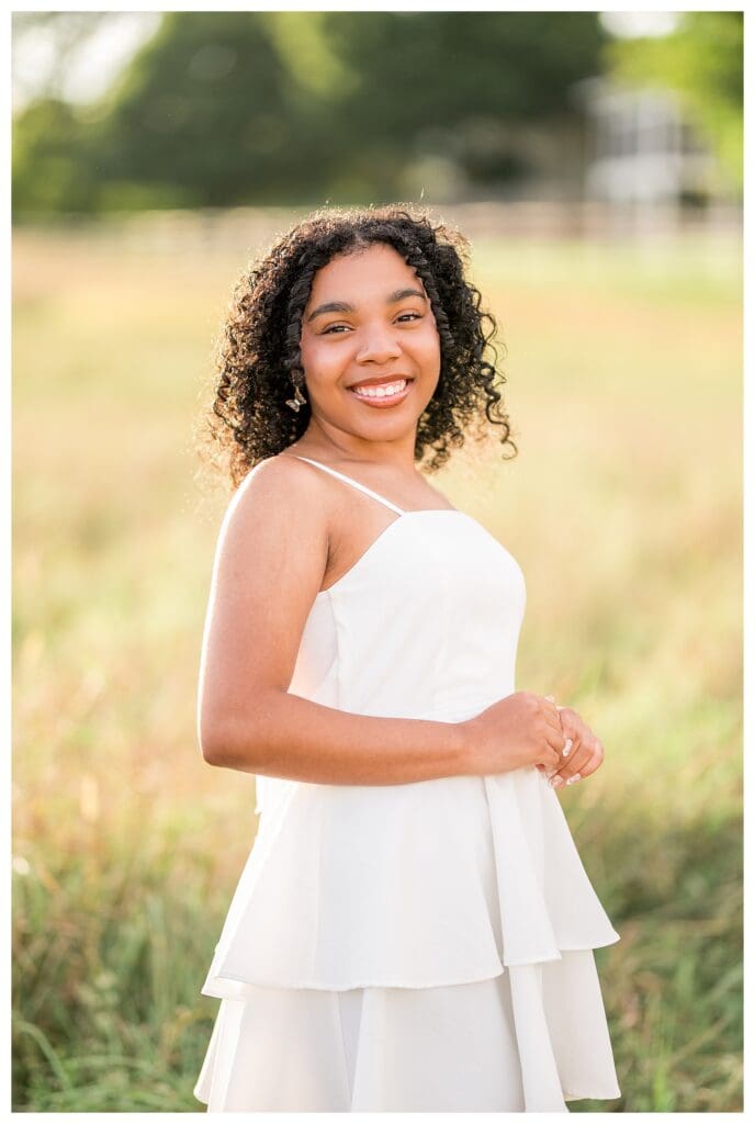 Curly haired senior smiling softly in close up portrait at golden hour.