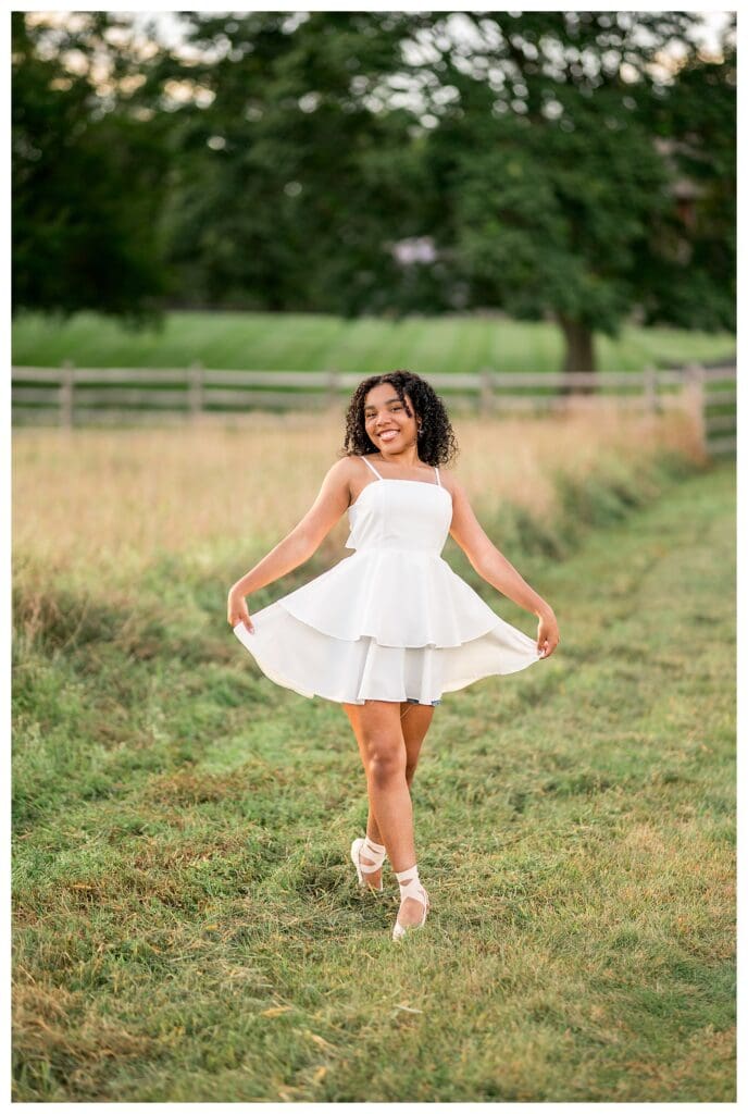 Senior balancing in pointe shoes in sunlit Massachusetts field.