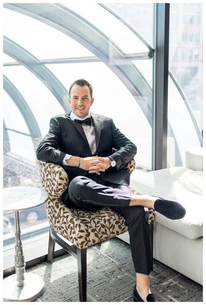 Groom portrait by window with Boston skyline in background.