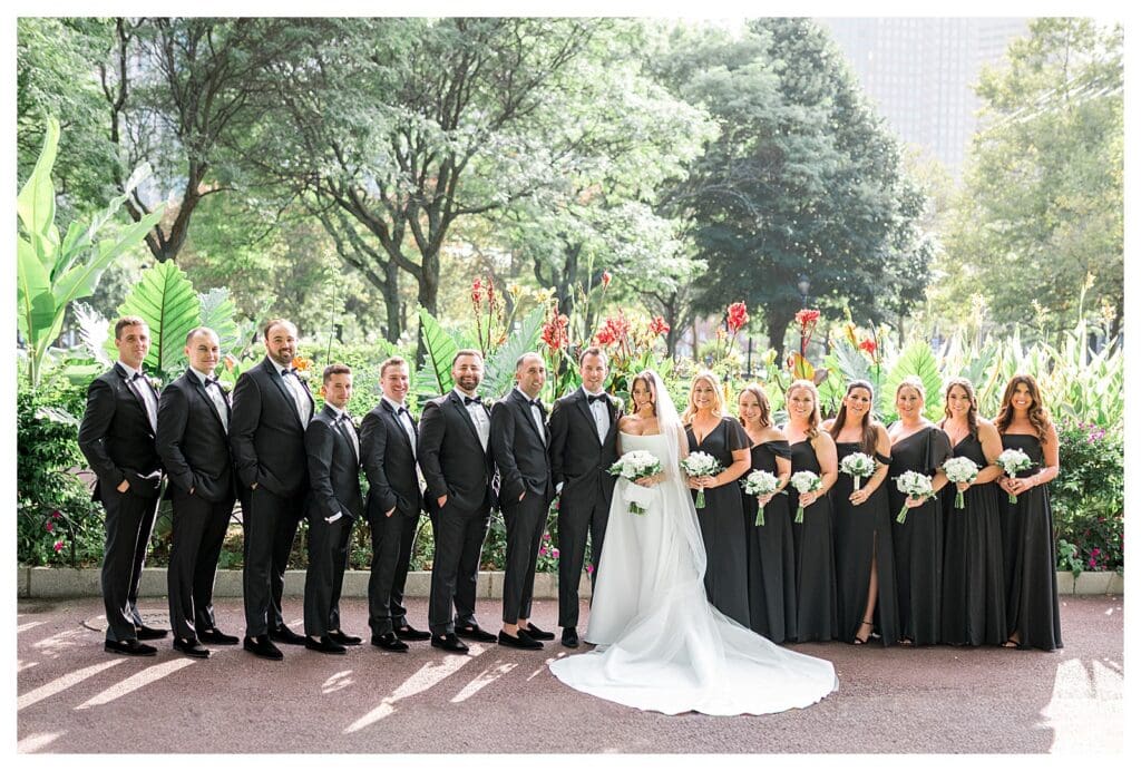 Wedding party lined up in black dresses and suits at Boston park.