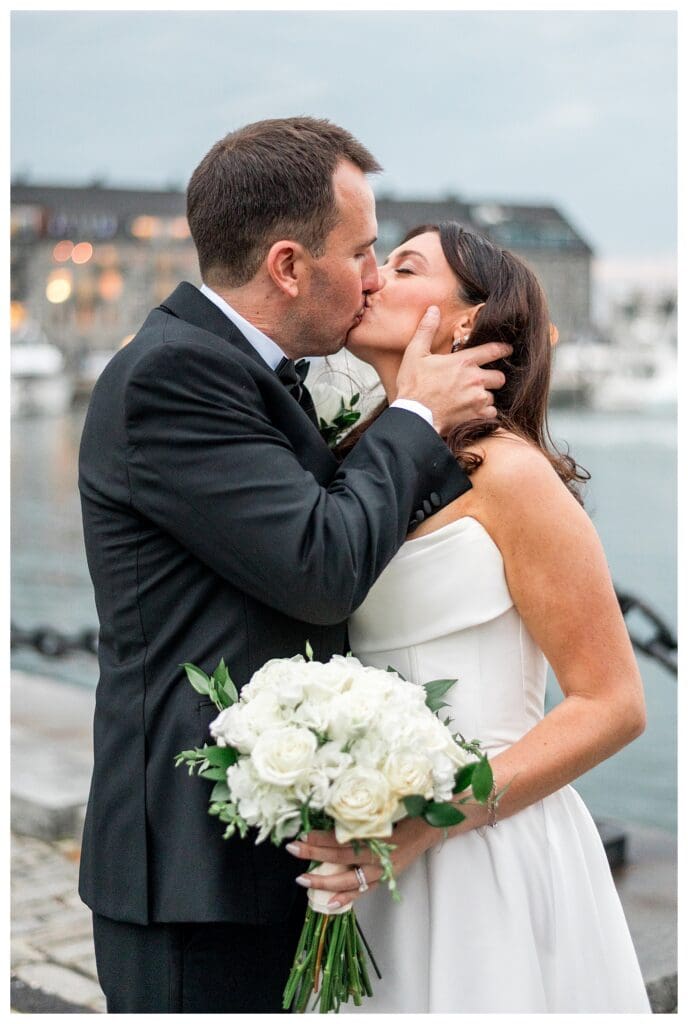 Romantic kiss by chain railing along Boston harbor.