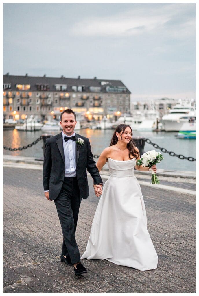 Bride and groom walking along Boston harbor waterfront on wedding day.
