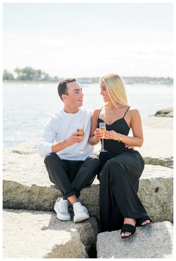 Newly engaged couple sitting on rocks toasting with champagne.