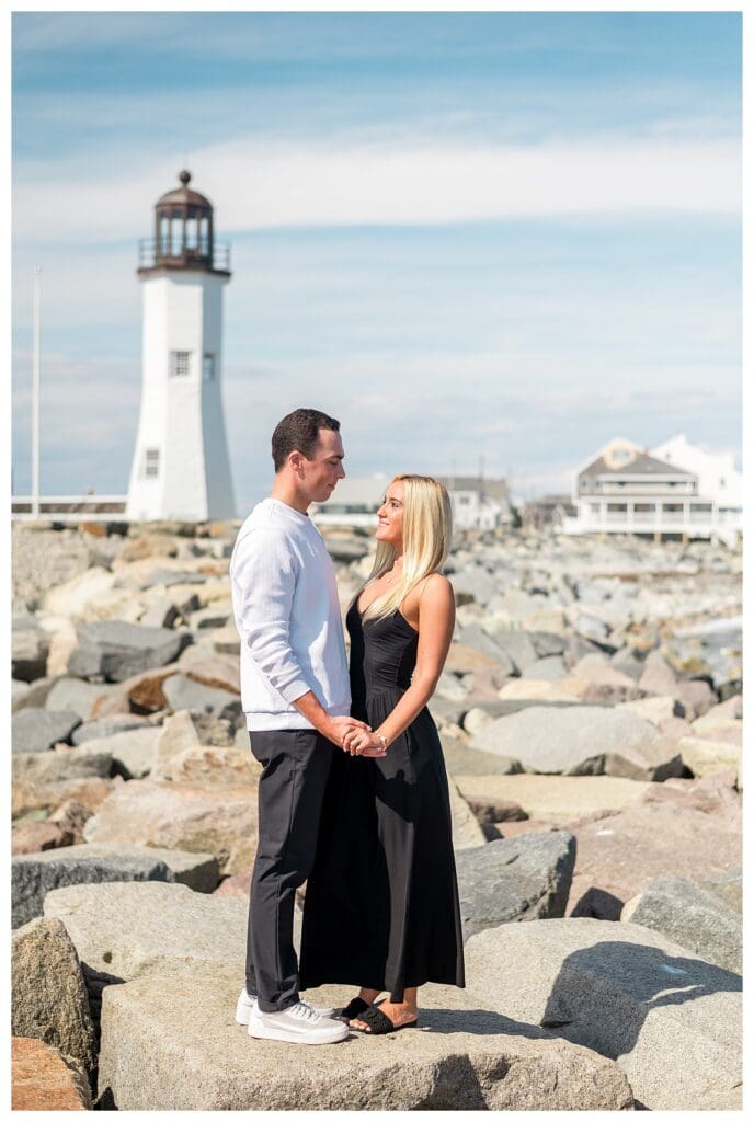 Full-length portrait of couple smiling with lighthouse and ocean backdrop.