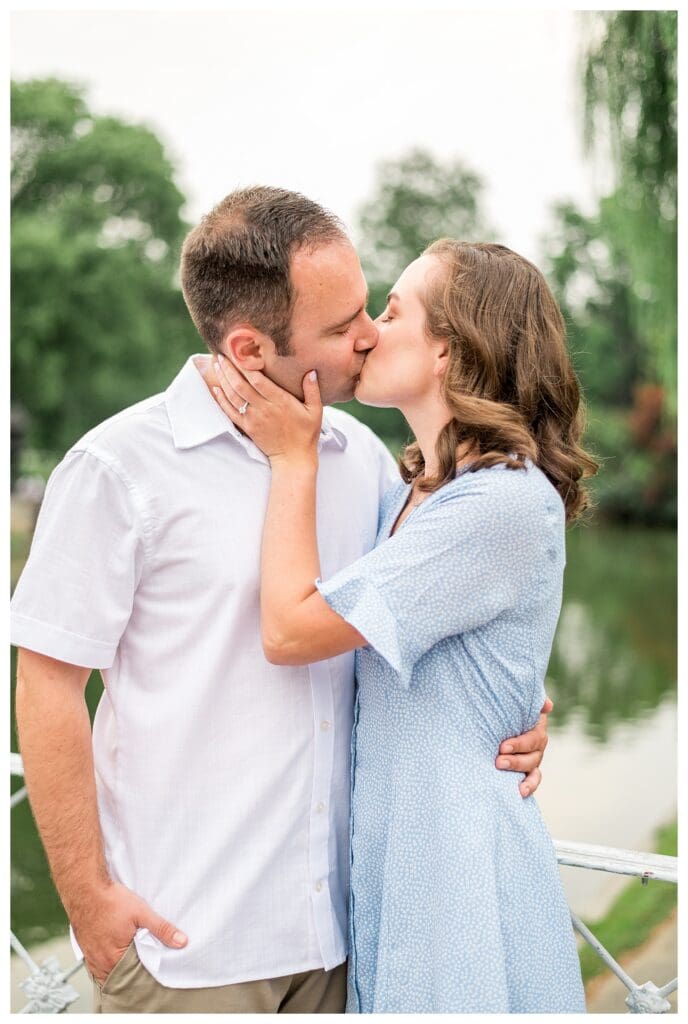 Couple sharing a romantic kiss during Boston engagement session with soft greenery