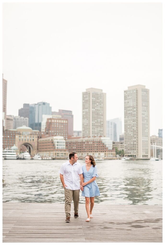 Couple walking along Seaport waterfront during Boston engagement session