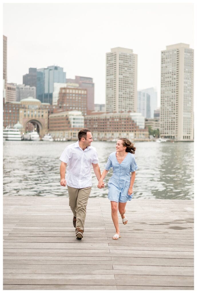Couple with Boston skyline behind them at Seaport waterfront engagement session