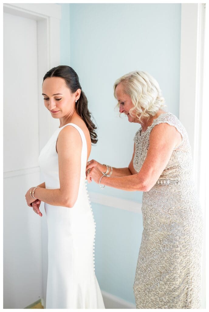 Mother helping bride get dressed at beachside wedding