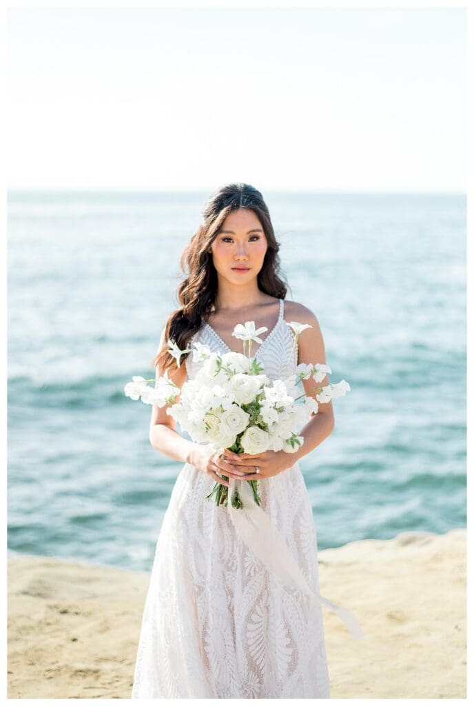 Bride standing alone on the coastline in white gown at Sunset Cliffs San Diego.