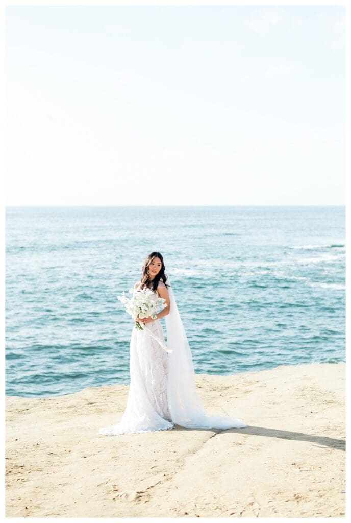 Bride in white gown holding white bouquet with ocean backdrop at Sunset Cliffs San Diego.