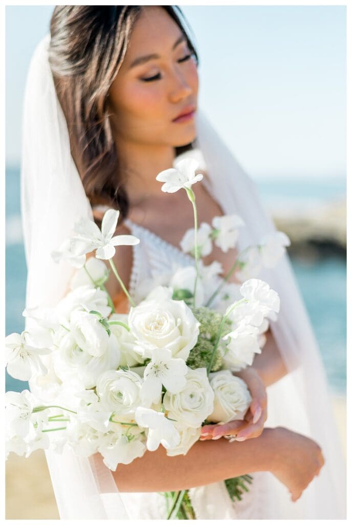 Bride holding white bouquet with Pacific Ocean behind her at Sunset Cliffs San Diego elopement.