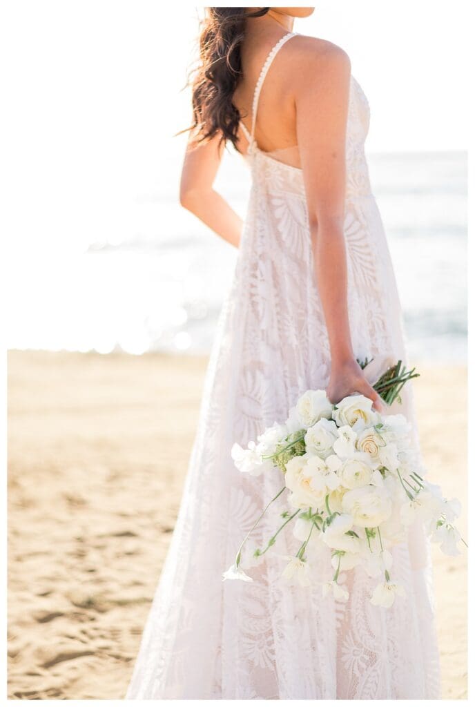 Bride in flowing white gown on sandy beach at Sunset Cliffs San Diego.
