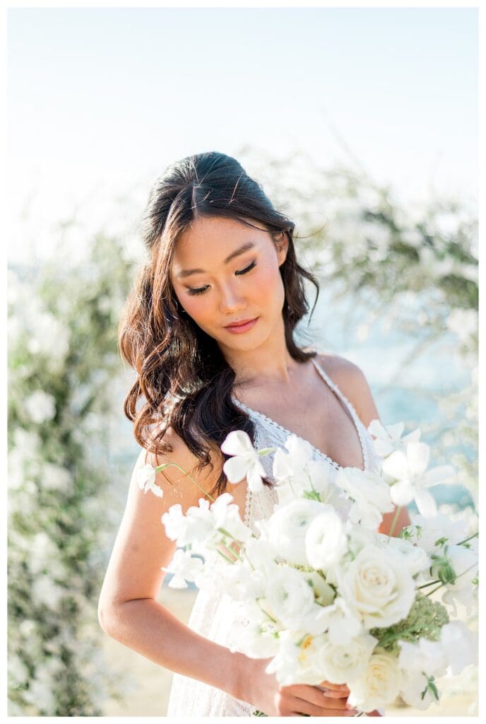 Bride looking down at bouquet near floral arch at Sunset Cliffs San Diego elopement.