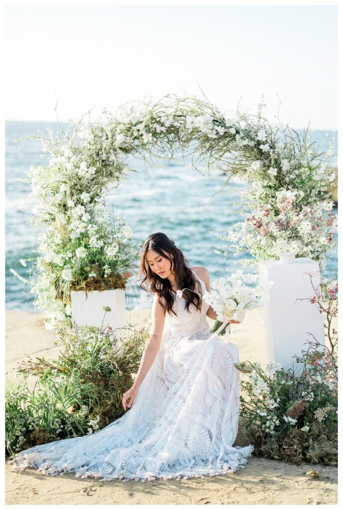 Bridal portrait at white floral arch with Pacific Ocean backdrop at Sunset Cliffs San Diego