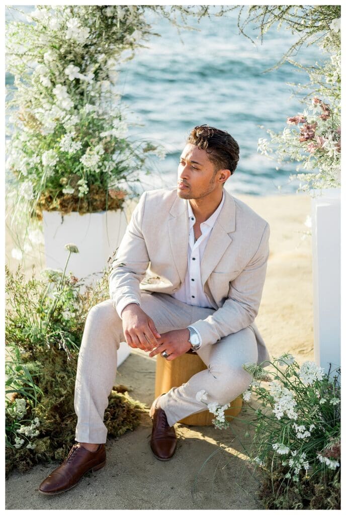 Groom in cream suit seated at Sunset Cliffs San Diego styled elopement shoot by Sarah Surette Photography