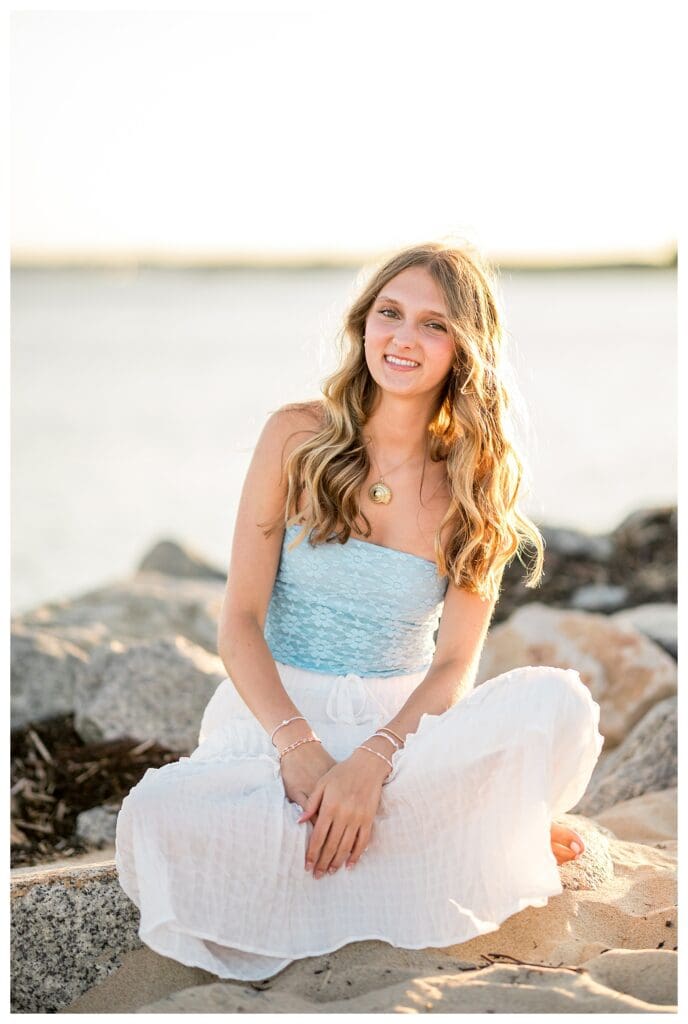 Senior girl sitting on rocks by the water in New England coastal senior photos.
