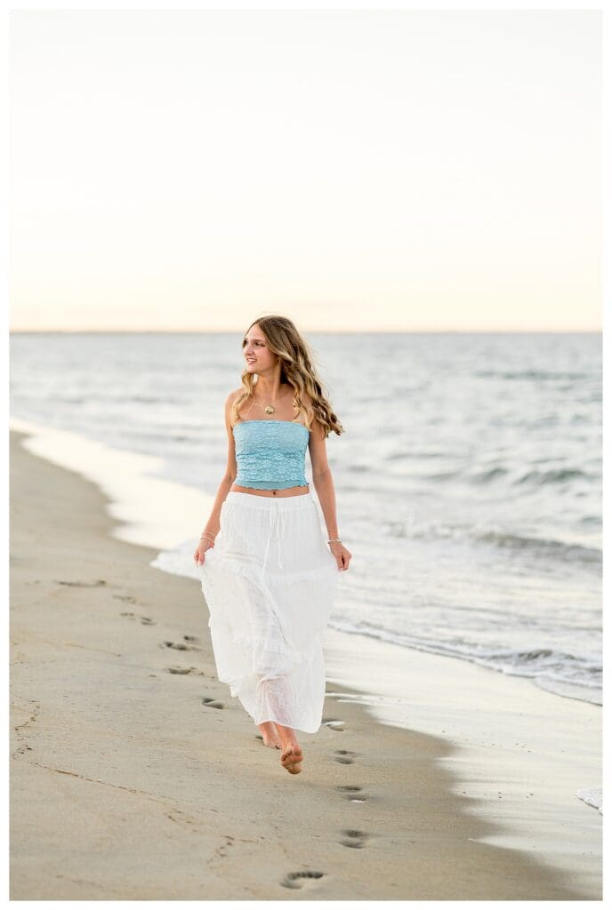 Senior girl walking on the sand in a blue top and white skirt, beach senior session