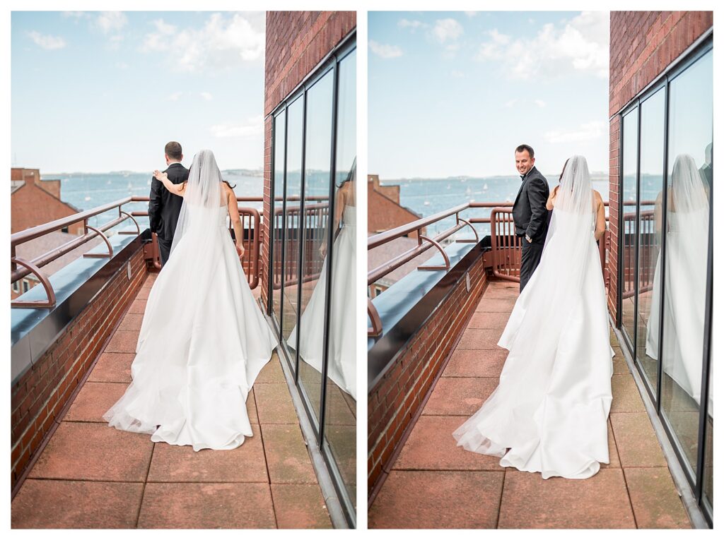Bride and groom standing on a rooftop terrace for their first look with Boston Harbor in the background, her veil blowing in the wind.