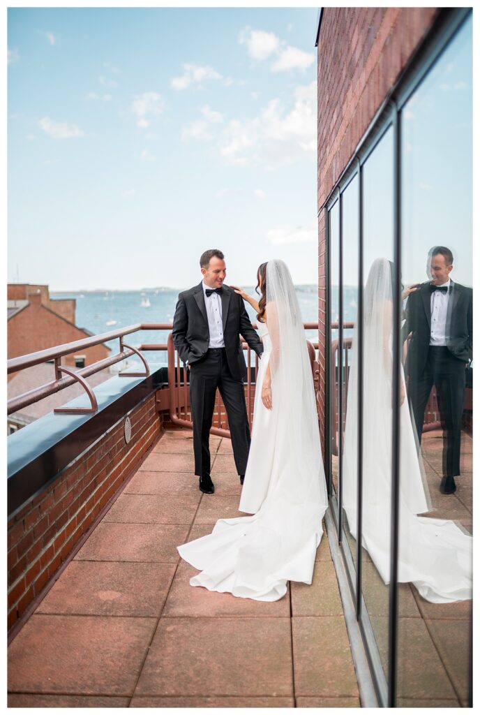 Wide shot of the bride and groom on a rooftop terrace overlooking the harbor and city skyline.