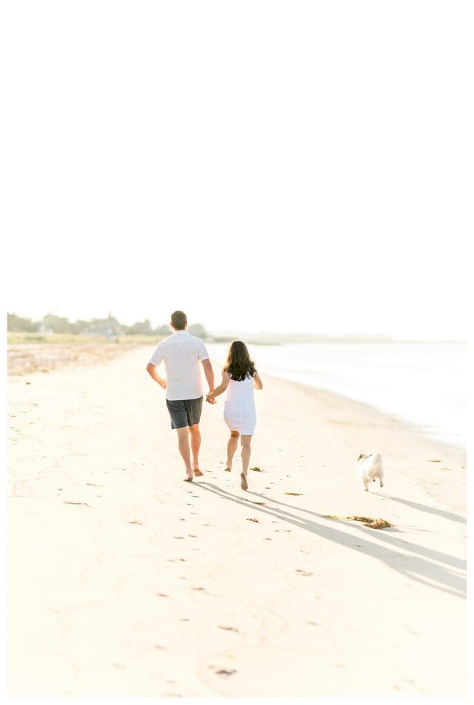 Dog running alongside engaged couple during a beach engagement session