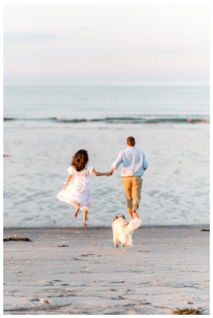 Running hand in hand toward the ocean with their dog