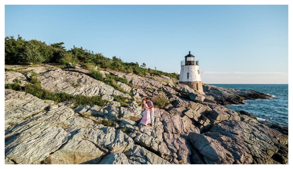 Couple stands together by the water in a wide shot of the Newport coastline.